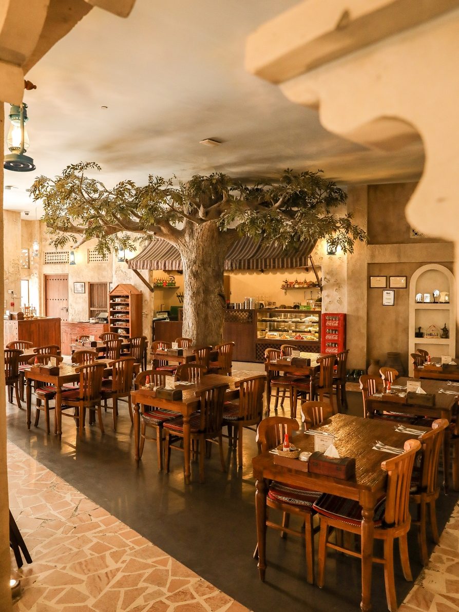 The dining courtyard at Yas Mall, with a great tree, carved plaster arches, lanterns and wooden tables