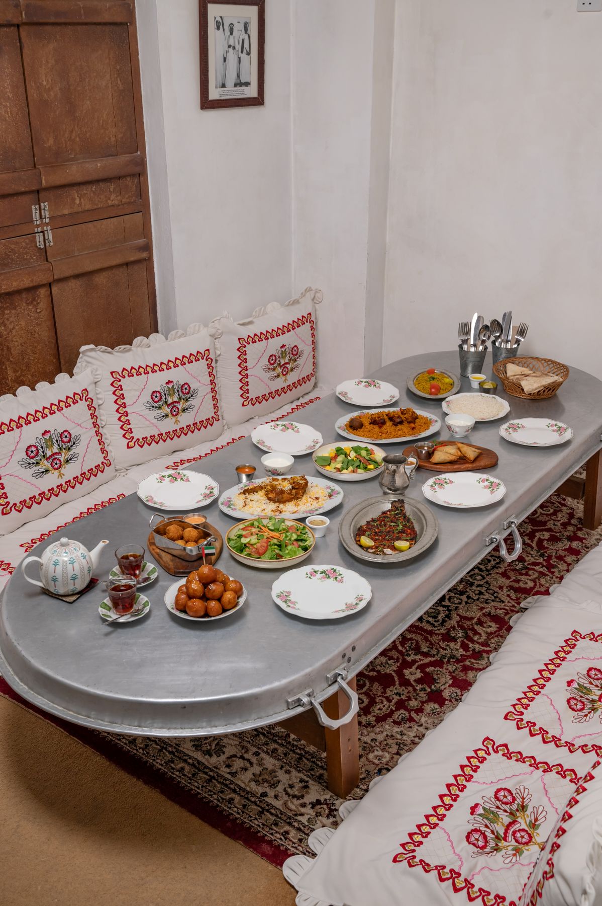 Floor seating with embroidered cushions around a low table of shared Emirati dishes